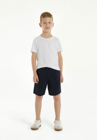 Bílý tričko s krátkým rukávem, námořnické šortky a bílé tenisky. Tkanina vypadá jemně, má volný střih a základní design.
