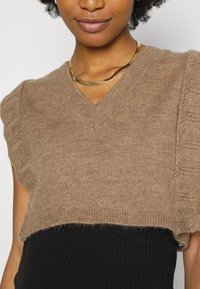 Top de malha castanho, de mangas curtas, com decote em V e bordas scallop, apresentando uma textura suave e uma silhueta cropped.