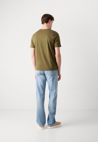 T-shirt en coton vert olive avec un col ras du cou, associé à un jean en denim bleu clair et des chaussures beige, vu de dos.