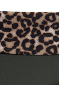 Lāču raksts audumā augšpusē ar brūnām un melnām nokrāsām, savienots ar vienmērīgu tumši zaļu pamataudumu. Tekstūras un kontrastējoši dizaina elementi.