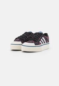 Svarta blommiga sneakers med vit tre-stripes-design, som har svarta snören, gummitröja och en texturerad vit sula med blå accenter.