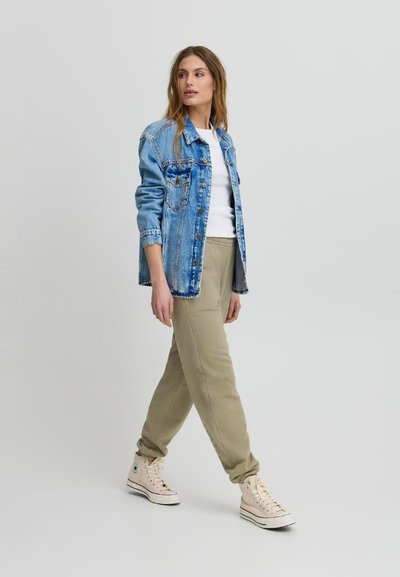 Denim jakna svijetloplave boje, u kombinaciji s bijelom majicom i bež trenirkama. Bež visoke tenisice upotpunjuju izgled.