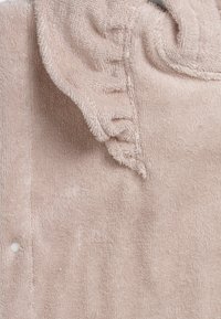 Ljust rosa frottétyg med volangdetalj vid halsringningen. Har knäppning med knappar och strukturerad yta. Lätt, mjukt material.