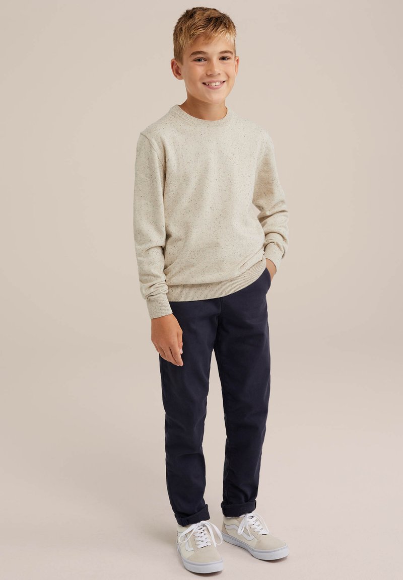 Ljus beige sweatshirt med ett fläckigt mönster, parat med marinblå byxor och grå sneakers. Sweatshirten har rund hals och ribbade manschetter.