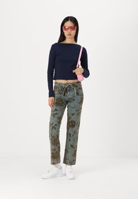 Jūrinės ilgomis rankovėmis crop top'o, raštuoti mėlyni džinsai su rudais gėlių motyvais, baltos sportbačiai ir rožinė rankinė per petį. Rožiniai saulės akiniai užbaigia išvaizdą.