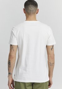 Hvit bomulls T-skjorte med rund hals og korte ermer, med en glatt tekstur og en etikett i sømmen. Minimalistisk design.