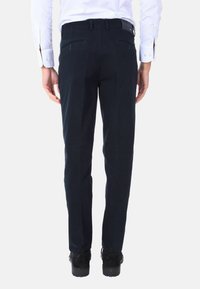 Pantaloni blu navy con vestibilità su misura, caratterizzati da una texture liscia e tasche posteriori. Abbinati a scarpe nere, visti da dietro.
