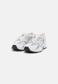Para białych i szarych sneakersów sportowych z siateczkowej tkaniny, sznurówkami i czarnymi gumowymi podeszwami, ustawionych obok siebie na białym tle.