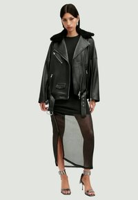 Μαύρο δερμάτινο μπουφάν μοτοσικλέτας με απομίμηση γούνας γιακά, στολισμένο πάνω από ένα μαύρο φόρεμα με διάφανο, ψηλό σκίσιμο και μεταλλικά τακούνια με λουράκι στον αστράγαλο.