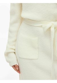 Krem kardigan od pletiva s teksturiranim materijalom, dugim rukavima, vezanim pojasom u struku i malim zakrpnim džepom sa strane.