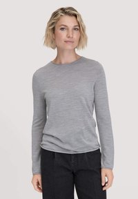 Lichtgrijze lange mouw shirt met een ronde hals, gemaakt van zachte stof, met een ontspannen pasvorm en subtiele textuur. Gepaard met donkere broek.
