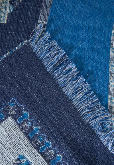 Couches de tissu tissé bleu et bleu marine avec des textures, motifs et bords à franges variés qui se chevauchent.