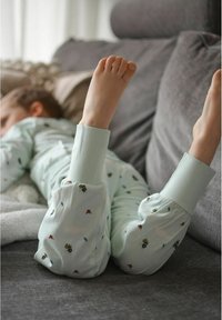 Ljust blå pyjamas-set med elastiska ärmslut, prydd med små, färgglada insektmönster. Mjuk tygtextur, barnets fötter synliga.