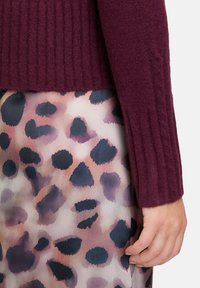 Bordeaux geribbelde trui gecombineerd met een gladde, gemusterde rok met abstracte luipaardvlekken in tinten roze, paars en zwart.