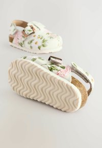 Weiße Clogs mit Blumenmuster in Rosa und Grün, ausgestattet mit einem Korkfußbett, verstellbarem Schnallenverschluss und einer strukturierten Gummisohle.