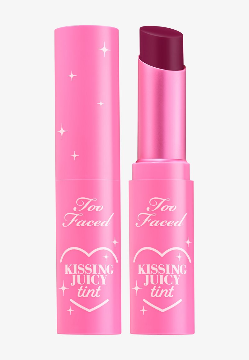 Roze lippenstift tube met een glanzende afwerking, versierd met decoratieve sterren. De dop onthult een diep bessenkleurige getinte lippenbalsem. Tekst: "Too Faced Kissing Juicy Tint."