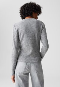 Gray knitted sweater with a round neck, long sleeves, and a textured finish. Paired with light gray jeans featuring back pockets.