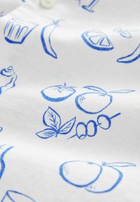 Tissu blanc avec des dessins en ligne bleue de divers fruits et légumes, y compris des tomates, des citrons et des herbes, dans un motif ludique.