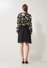 Svart klänning med en broderad blommönster i guld och vitt, med långa ärmar och elastisk midja, som slutar ovanför knäet.