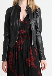 Czarna skórzana kurtka o dopasowanym kroju, z prążkowanym kołnierzem i zamkiem błyskawicznym. Gładka faktura z minimalną ilością detali metalowych.