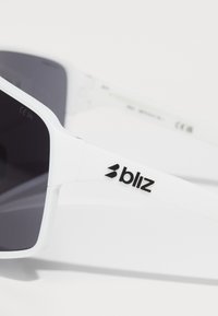 Fehér napszemüveg téglalapkerettel, sötét lencsékkel és matt felülettel. A szárán fekete "bliz" logó található.