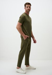 Olijfgroen T-shirt met korte mouwen, gecombineerd met bijpassende taps toelopende broek. De stof ziet er zacht uit. Heeft zijzakken en witte sneakers.