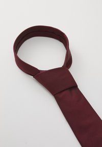 Cravat din mătase roșie închisă, legată cu un nod Windsor, așezată pe un fundal alb.