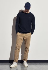 Pull en maille marine, chinos kaki et baskets blanches. L'ensemble est rehaussé d'une casquette de baseball. Les matériaux semblent décontractés et confortables.