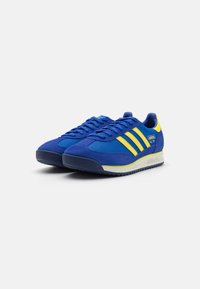 Blauwe suède sneakers met mesh accenten, gele strepen en een gemarmerde rubberen zool. Voorzien van een zachte tong en een gevoerde hakontwerp.