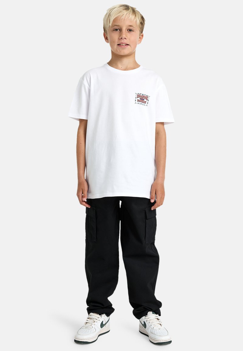 T-shirt bianca in cotone con una stampa sul petto, abbinata a pantaloni cargo neri e sneakers bianche con dettagli verdi.