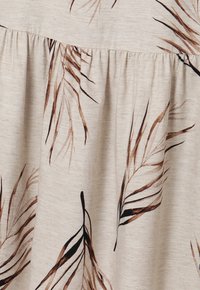 Tissu beige avec des fronces et des impressions de feuilles de palmier marron et noires réparties sur le matériau.