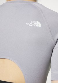 Primer plano de una camiseta deportiva gris con el logotipo blanco de The North Face en la parte superior de la espalda y una sección recortada por encima de la cintura.