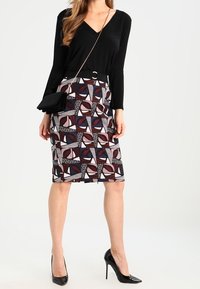 Czarna bluzka z długim rękawem w połączeniu z dopasowaną spódnicą do kolan z geometrycznymi wzorami w kolorach bordo, granatowym, białym i czarnym.
