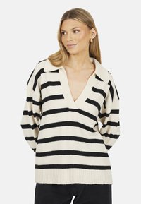 Maglione crema con righe nere orizzontali, colletto a V, taglio loose fit e orlo a costine. Materiale in maglia morbida e testurizzata.