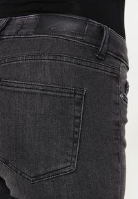 Musta farkkushuihka, jossa on sileä tekstuuri, taka-tasku ja nahkainen brändilogo vyötäröllä. Puhtaat ompeluyksityiskohdat.