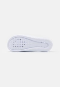 White rubber shoe sole featuring a textured surface with circular and hexagonal patterns, including a logo detail near the heel.