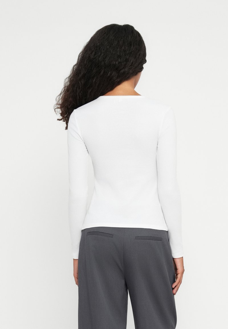 Haut à manches longues blanc côtelé avec un col rond, associé à un pantalon gris taille haute avec deux poches arrière et une texture lisse.