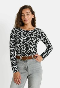 T-shirt noir à manches longues avec un motif abstrait blanc, col rond et coupe près du corps, associé à un jean gris taille haute et une ceinture marron.