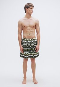 Ανδρικά μαγιό σορτς με ζιγκ-ζαγκ σχέδιο σε πράσινο, μαύρο και λευκό. Διαθέτουν ελαστική μέση και μήκος έως το γόνατο. Ελαφρύ ύφασμα.