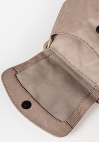 Interno di una borsa in pelle color beige chiaro con una texture liscia, dotato di una chiusura a bottone nero singolo e bordi cuciti. Aperta, rivela la fodera morbida.