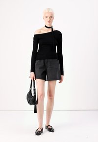 Zwarte off-the-shoulder lange mouw top, gecombineerd met grijze denim shorts. Model draagt een kleine zwarte handtas en heeft zwarte schoenen met accenten aan.