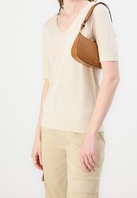 Maglione beige a maniche corte con scollatura a V, abbinato a pantaloni cargo color khaki. Borsa a spalla color beige con forma curvata e dettagli in oro.