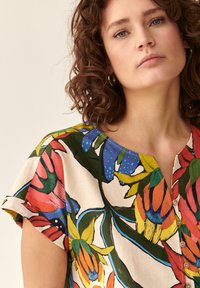 Bluză florală dintr-o țesătură ușoară, cu un model multicolor ce include frunze și flori, guler rotund și mâneci scurte.