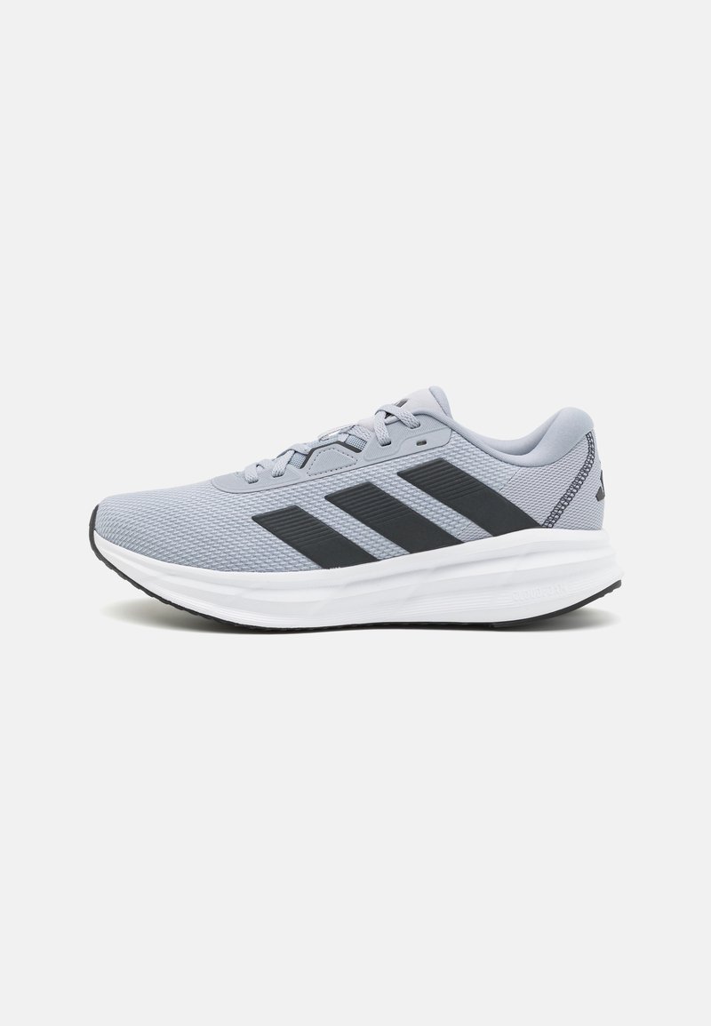 Chaussure de sport gris clair avec des rayures noires, semelle blanche et lacets, vue de côté sur un fond blanc uni.