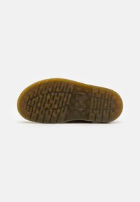 Shoe sole featuring a rugged, textured rubber design in brown and yellow, with a patterned grip and logo embossed on the surface.