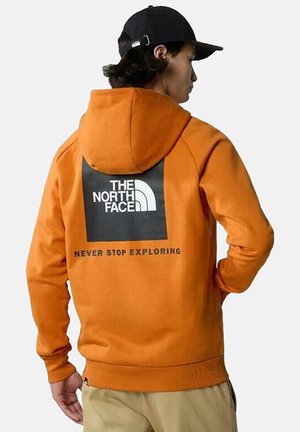 Sudadera naranja con capucha, detalle negro en la parte posterior con el logo "THE NORTH FACE" y el texto "NEVER STOP EXPLORING". Textura suave.
