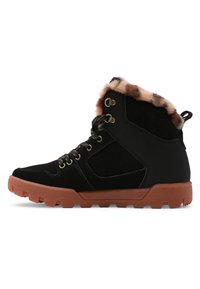 Botas de tobillo de ante negro con forro de piel de pelo, acentos beige, suela de goma marrón y ojales dorados para los cordones, con un cuello acolchado.