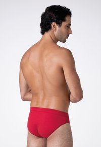 Culotte rossa in cotone con una superficie liscia, cinturino elastico e design minimalista, esposta su un modello visto da dietro.