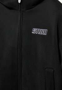 Fekete hálós cipzáras dzseki kis „STWD” fehér hímzett logóval a bal mellrészen, alul jobb oldalon látható zsebbel.