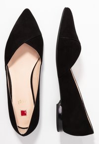 Bailarinas de ante negro con punta afilada y tacón bajo, que presentan un diseño recortado y una plantilla en contraste beige. Textura suave y estilo minimalista.